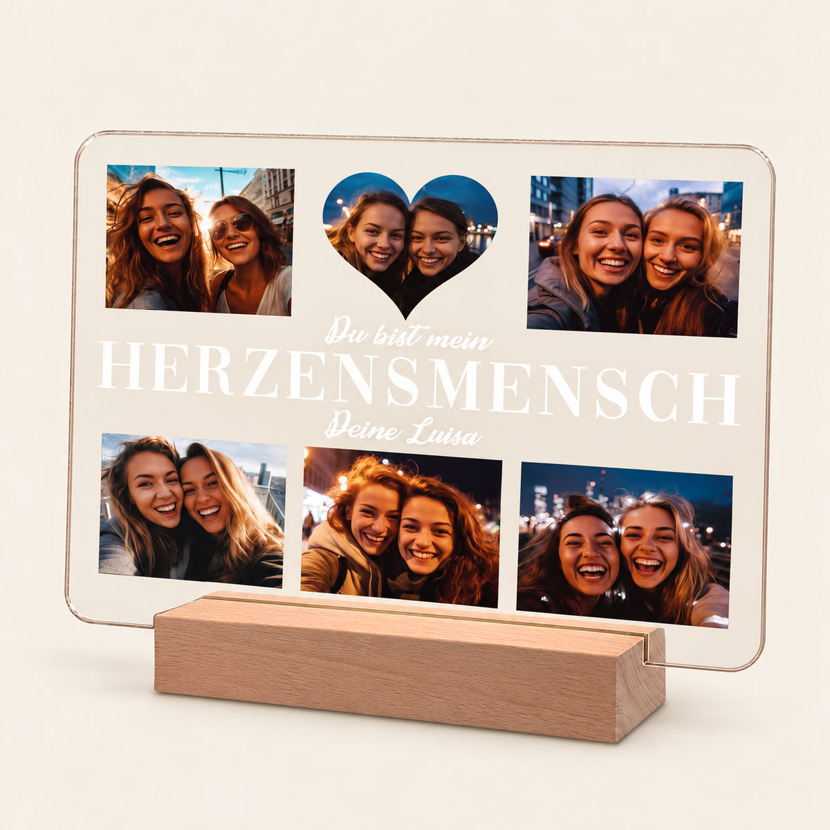 Beleuchtete Acryl‑Fotoanzeige auf einem Holz‑LED‑Ständer, mit fünf Freund‑Selfies um eine herzförmige Aussparung angeordnet. Weißer deutscher Text lautet 'Du bist mein HERZENSMENSCH - Deine Luisa'. Warmes Hintergrundlicht leuchtet durch das Panel.
