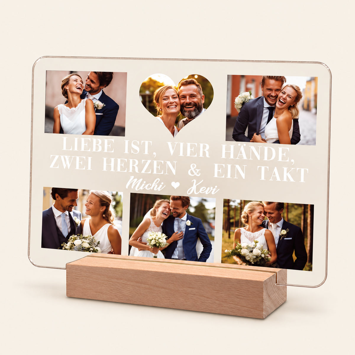 Personalisierte Acryl-Fotodarstellung auf einem hellen Holz-LED-Ständer, die sechs Hochzeitspaar-Fotos rund um ein herzförmiges Bild in der Mitte anordnet. Weißer deutscher Text lautet „Liebe ist, vier Hände, zwei Herzen & ein Takt“ mit den Namen „Michi & Kevi“ darunter.